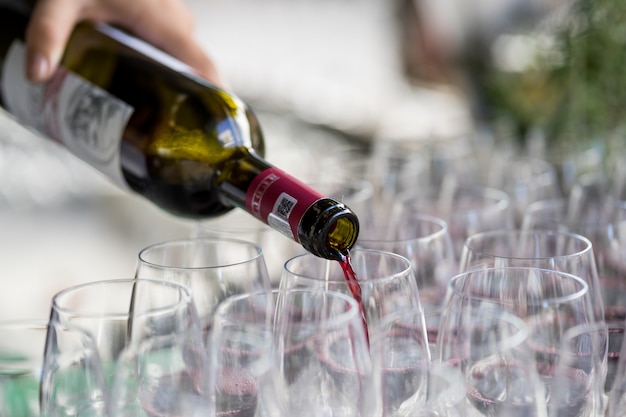 Primer plano de la mano con una botella de vino vertiendo vino en vidrio