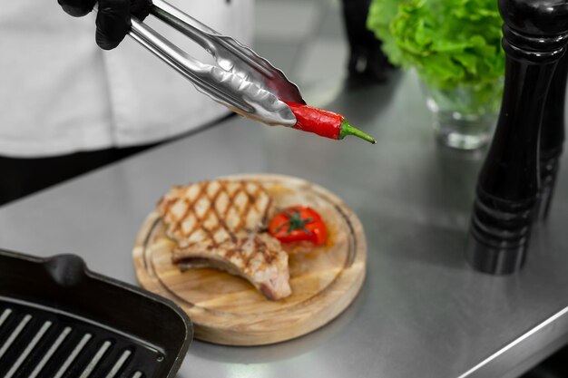 Primer plano de la mano del chef mientras pone chiles de la parrilla en un plato con un par de pinzas