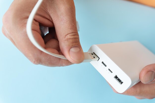 Foto un primer plano de una mano conectando un cable usb a un banco de energía blanco sobre un fondo azul