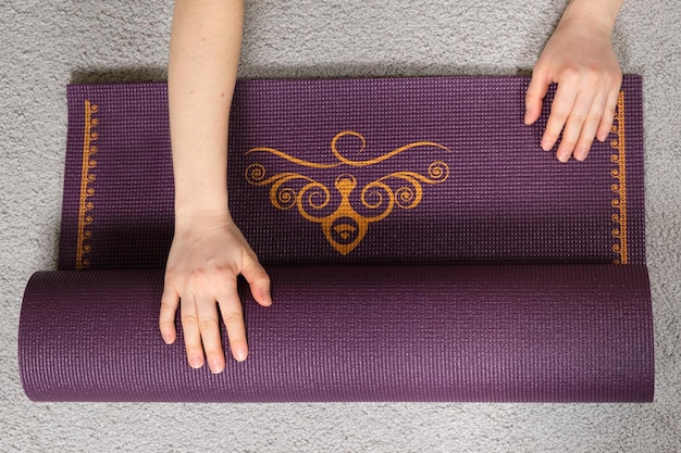 Un primer plano de una mano despliega una alfombra morada para yoga o fitness