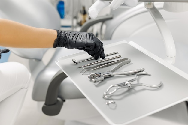 Primer plano de la mano de las doctoras en guante negro tomando instrumentos dentales de la bandeja durante el examen médico