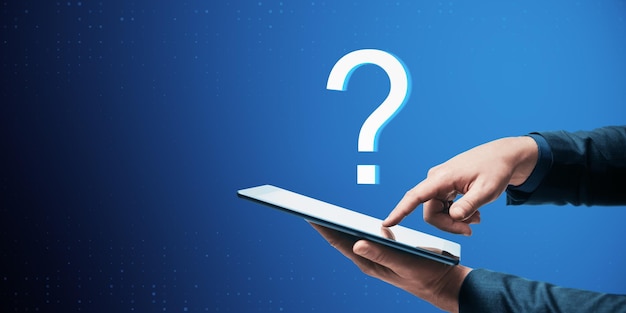 Primer plano de la mano del empresario apuntando a la tableta con un signo de interrogación digital abstracto sobre fondo azul Concepto de soporte y ayuda