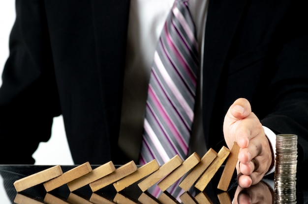 Foto primer plano de la mano del empresario detener bloques de madera de caer en monedas apiladas sobre escritorio