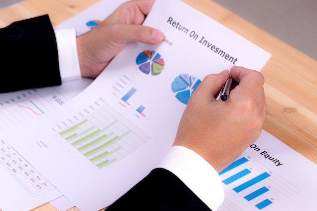 Primer plano de la mano del empresario que sostiene un documento en papel del informe financiero del retorno de la inversión