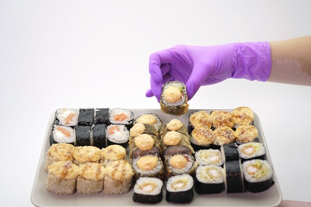 Primer plano de la mano enguantada de una mujer que presenta los rollos de sushi en un plato, pared aislada