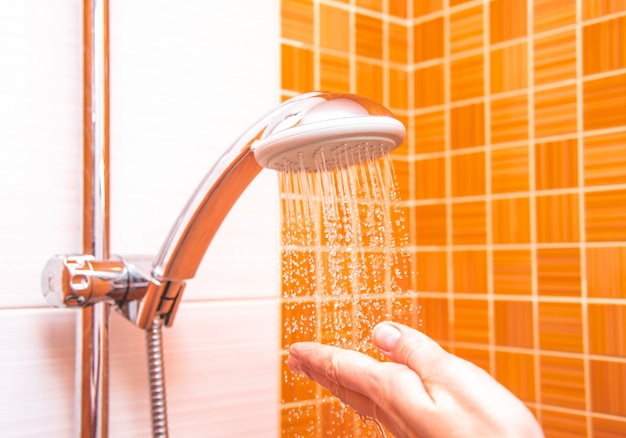 Primer plano de una mano femenina comprueba la temperatura del agua en la ducha