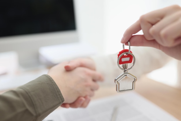 Primer plano de la mano femenina dando llaves al nuevo propietario de la casa firmando contrato y apretón de manos real