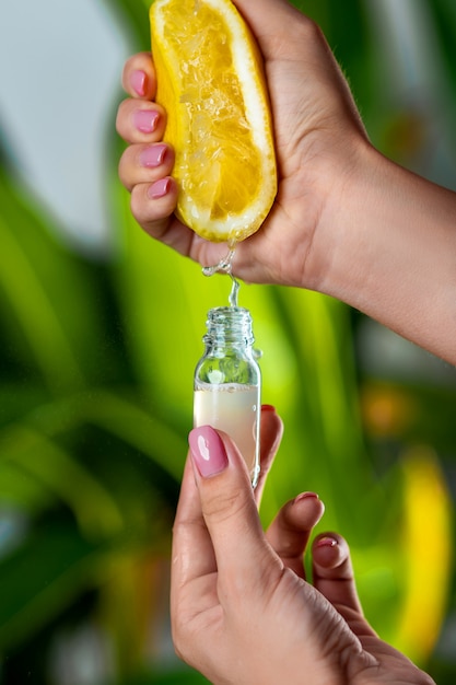 Primer plano: una mano femenina exprime el jugo de un limón en una botella de vidrio. La cosmética natural.