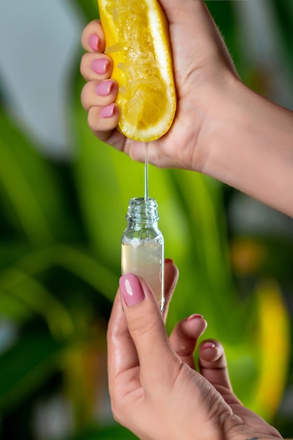 Primer plano: una mano femenina exprime el jugo de un limón en una botella de vidrio. La cosmética natural.