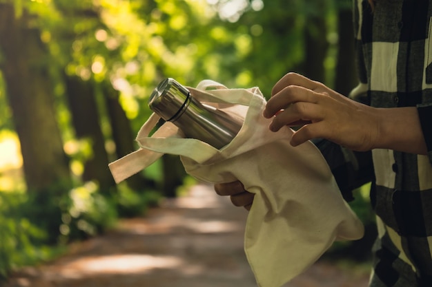 Primer plano de una mano femenina irreconocible sosteniendo una botella de agua de una bolsa ecológica Agua termo de acero reutilizable