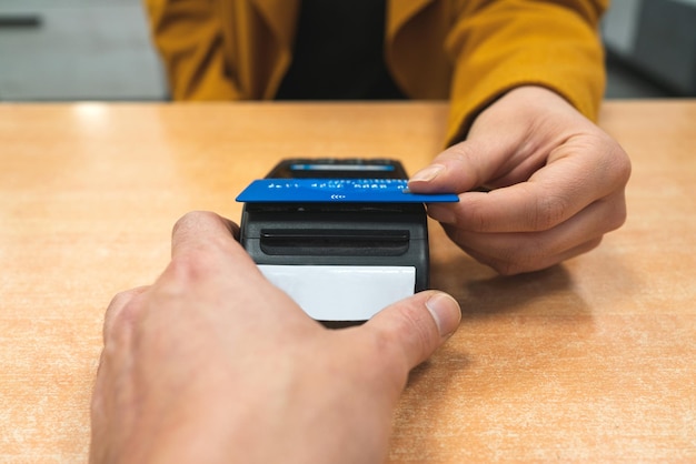 Primer plano de una mano femenina pagando con su tarjeta en un terminal POS o teléfono latafono en una tienda