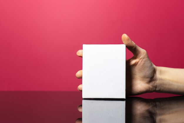 Primer plano de la mano femenina que sostiene la tarjeta de papel blanco con maqueta en la superficie de coral rosa