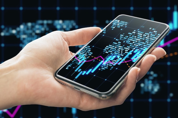 Primer plano de la mano femenina que sostiene el teléfono celular con un holograma de mapa de gráfico de forex de candelabro brillante sobre fondo oscuro Concepto de comercio y mercado