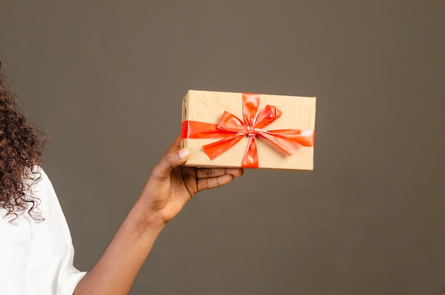 Primer plano de una mano femenina sosteniendo una caja de regalo aislada sobre un fondo gris