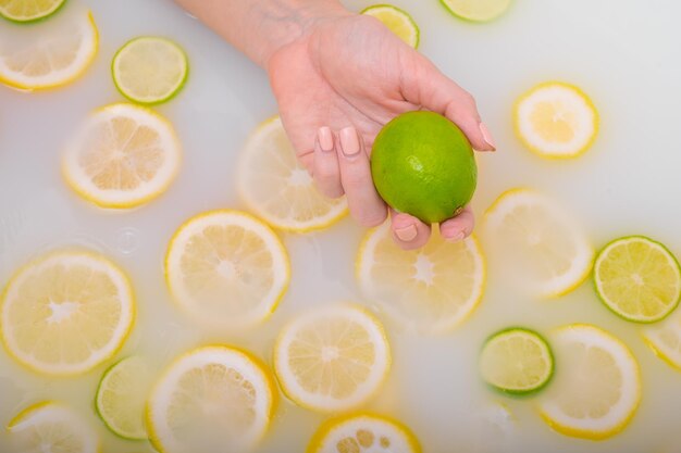 Primer plano de una mano femenina sosteniendo una lima sobre agua blanca con rodajas de limón