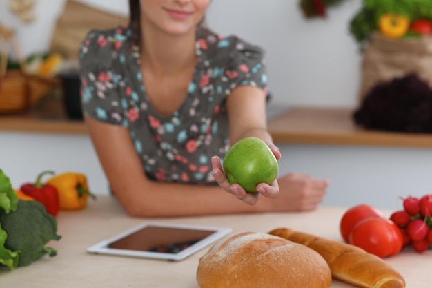 Primer plano de una mano femenina sosteniendo una manzana verde en los interiores de la cocina Muchas verduras y otras comidas en la mesa de cristal están listas para ser cocinadas pronto