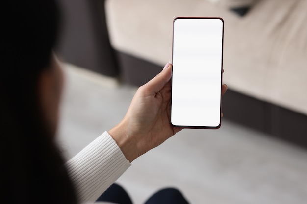 Foto primer plano de una mano femenina sosteniendo el teléfono móvil con pantalla en blanco