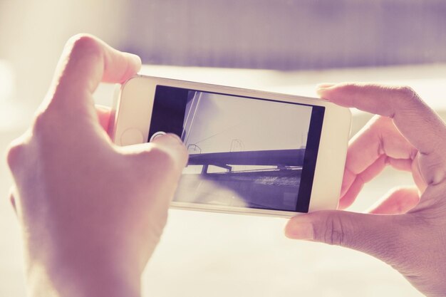 Foto primer plano de la mano fotografiando el puente a través de un teléfono móvil