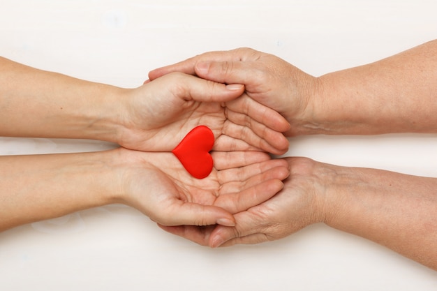 Foto primer plano de la mano de una hija adulta y una madre mayor sosteniendo un corazón juntos