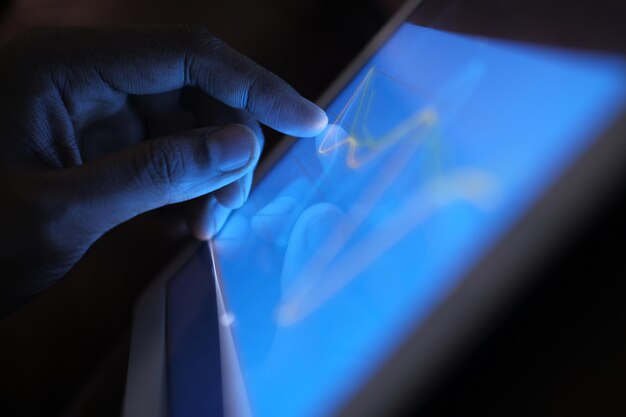 Un primer plano de la mano del hombre analizando el gráfico en una tableta digital