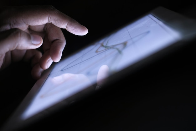 Un primer plano de la mano del hombre analizando el gráfico en una tableta digital