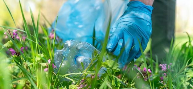 Primer plano de la mano de un hombre con guantes de goma recogiendo residuos plásticos en la naturaleza