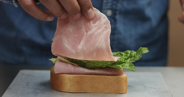 Primer plano de la mano del hombre haciendo sándwich pone de los lados todos los ingredientes en el plato