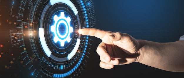 Primer plano de la mano del hombre de negocios que señala el holograma creativo de la rueda dentada que brilla intensamente sobre fondo oscuro El progreso empresarial y el concepto de tecnología