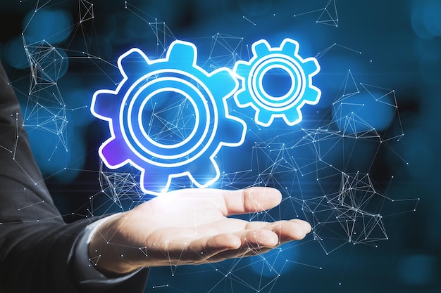 Primer plano de la mano de un hombre de negocios sosteniendo ruedas de engranajes brillantes abstractas en un fondo bokeh azul con conexiones Concepto de ingeniería digital e industria