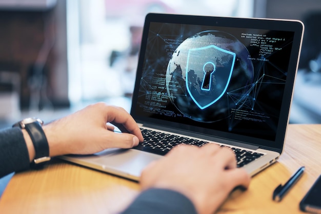 Foto primer plano de la mano del hombre de negocios usando el teclado de la computadora portátil en el escritorio de madera con holograma de seguridad abstracto con globo y codificación sobre fondo borroso protección segura y concepto web doble exposición