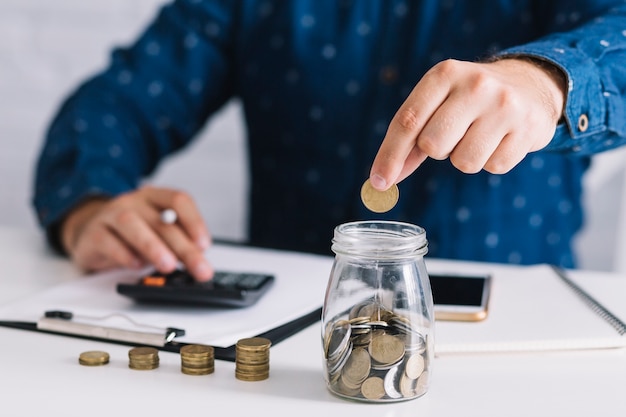 Foto primer plano de la mano del hombre poniendo la moneda en el vaso con calculadora