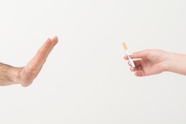 Foto primer plano de la mano de un hombre que dice no al cigarrillo dado por una persona aislada en el fondo blanco