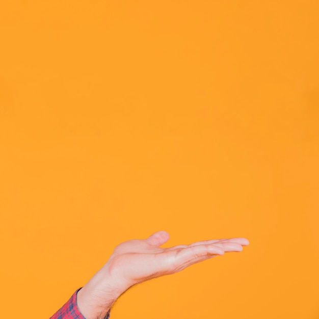 Foto primer plano de la mano del hombre que presenta algo contra un fondo naranja