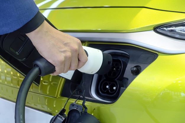 Primer plano de la mano del hombre que sostiene un enchufe de máquina recargable para el cargador de batería en el enchufe del coche eléctrico blanco