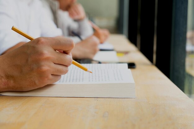 Foto primer plano de la mano de un hombre sosteniendo un lápiz de color amarillo mientras lee un libro