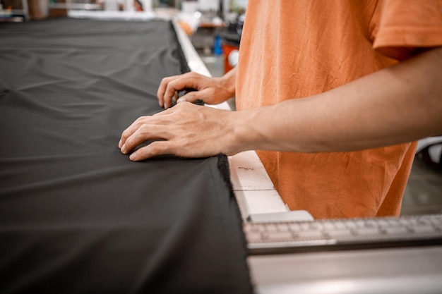Primer plano de la mano del hombre tendido de tela Tomada en la fábrica Proceso de trabajo de la fábrica de telas textiles Equipo de trabajadores de sastrería