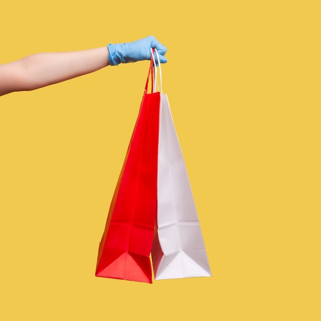 Primer plano de una mano humana en guantes quirúrgicos azules sosteniendo y mostrando el bolso de compras rojo y blanco.