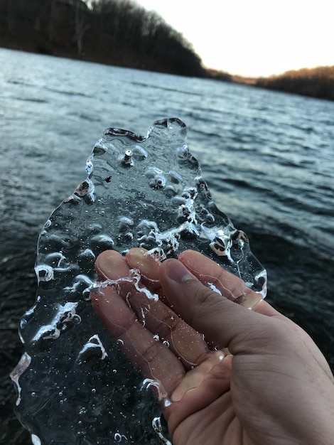 Foto primer plano de una mano humana sosteniendo el hielo contra el lago