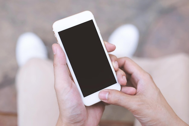 Primer plano de la mano de un joven sosteniendo un teléfono móvil inteligente con pantalla de teléfono celular vacío sentado en una silla en un parque público al aire libre Vista superior con espacio para copiar