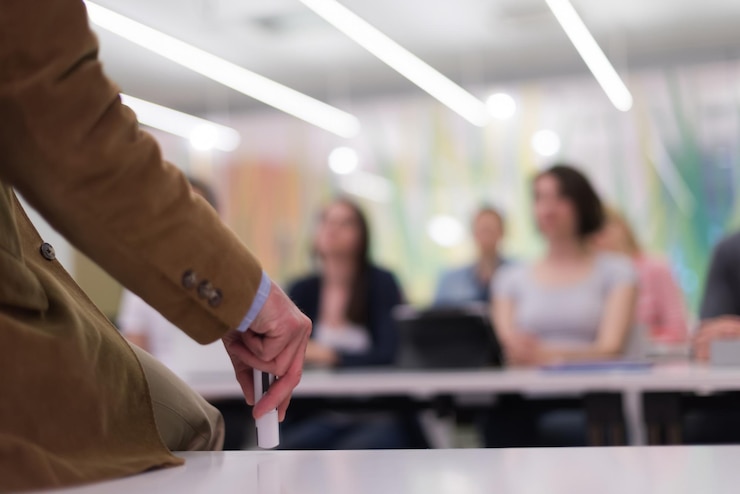 Foto primer plano de la mano del maestro con marcador mientras enseña lecciones en el aula de la escuela a los estudiantes