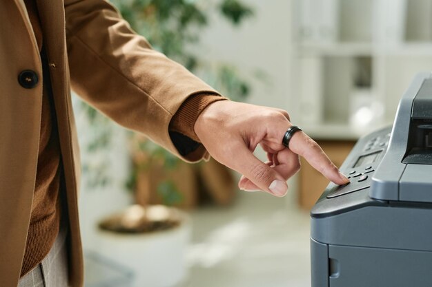 Primer plano de la mano masculina en el anillo presionando el botón del escáner mientras se trabaja con documentos en la oficina