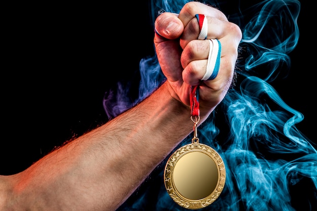 Primer plano de una mano masculina fuerte que sostiene una medalla de oro para un logro deportivo