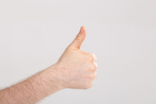 Primer plano de una mano masculina mostrando los pulgares hacia arriba sobre la pared blanca con espacio de copia