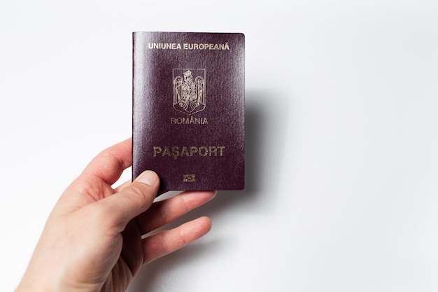 Primer plano de una mano masculina con pasaporte rumano en la mano sobre fondo blanco