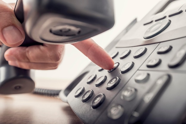 Foto primer plano de la mano masculina que sostiene el receptor de teléfono mientras marca un número de teléfono