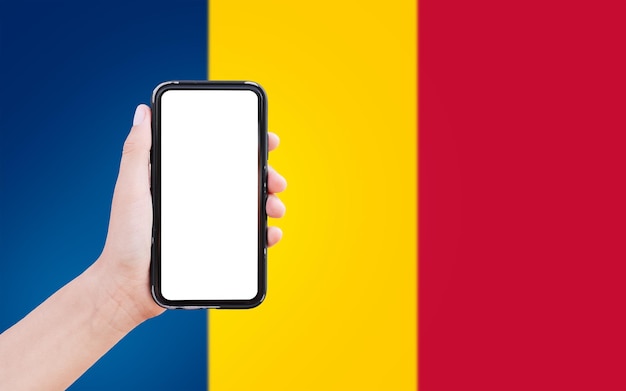 Primer plano de la mano masculina que sostiene el teléfono inteligente con pantalla en blanco en el fondo de la bandera borrosa de Chad