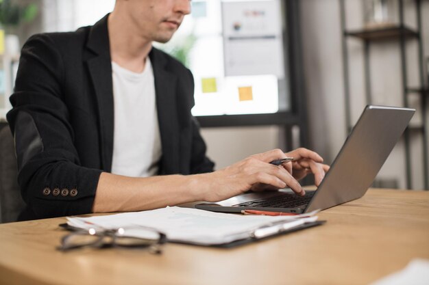 Primer plano de la mano masculina en ropa formal escribiendo en una computadora portátil moderna mientras está sentado en el escritorio