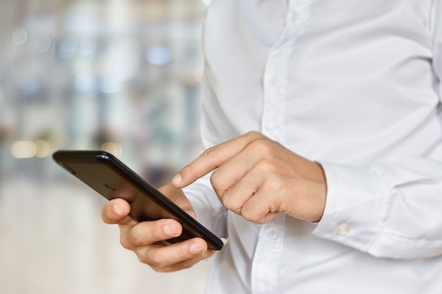 Primer plano de la mano masculina con smartphone. Empresario toque teléfono móvil con fondo bokeh. Enfoque selectivo en mano.