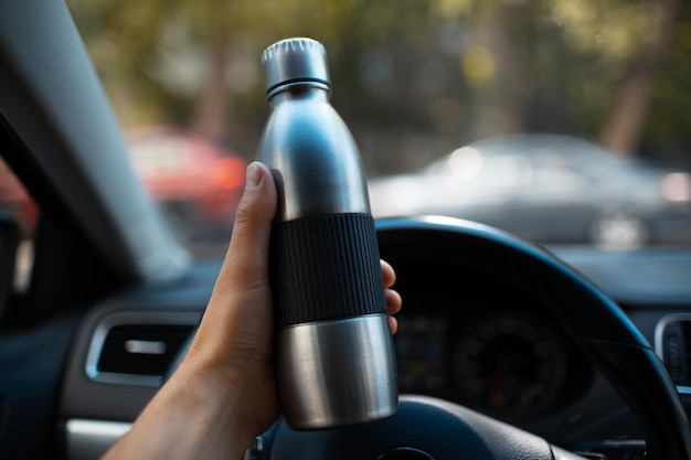 Primer plano de una mano masculina sosteniendo una botella de agua reutilizable de acero dentro del automóvil