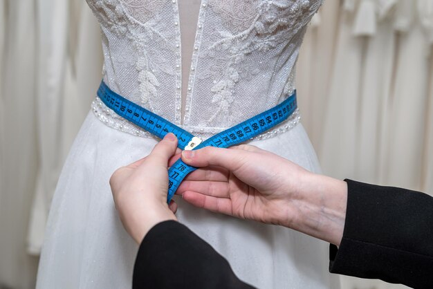 Primer plano de la mano de la modista de diseñadora que ajusta el vestido de novia con cinta métrica en la boutique